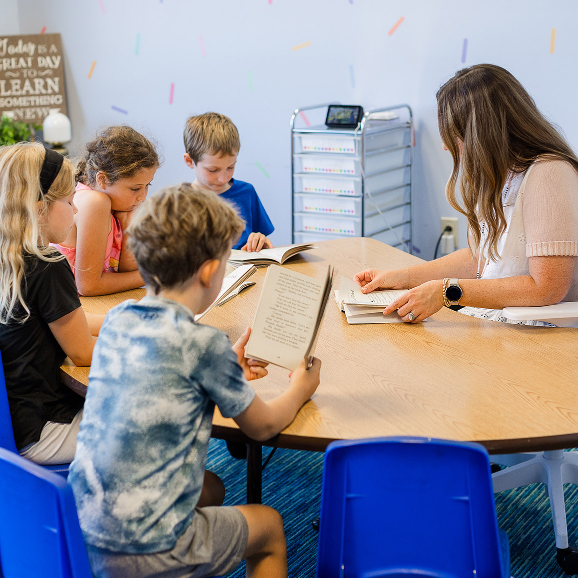 Students reading a book a loud while together sitting around the teacher at a table