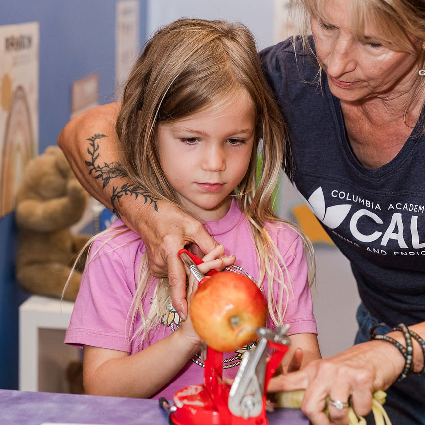 Teacher working with student to teach her how to peel an apple