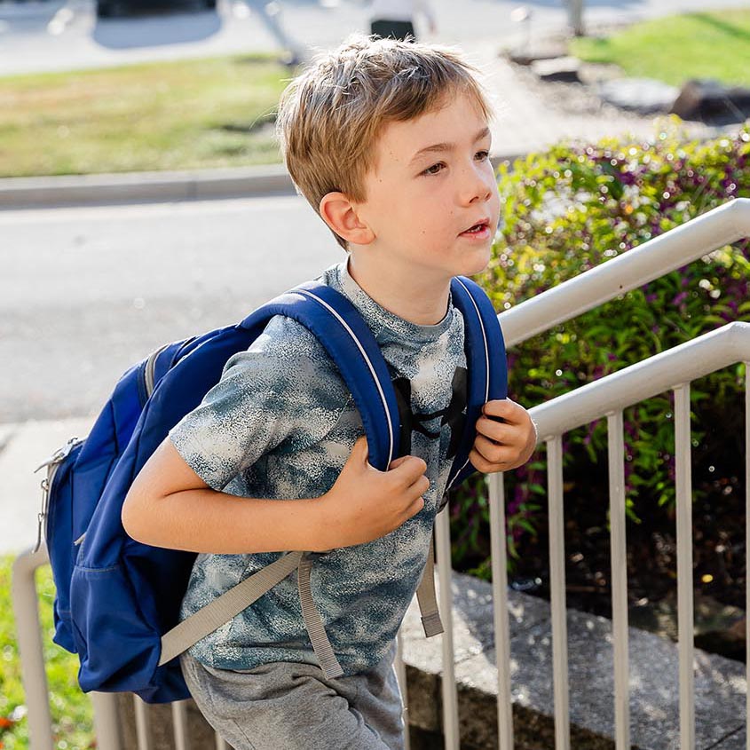 Young student walking into school holding his backpack straps